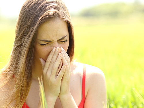 Woman sneezing in a field due to allergies
