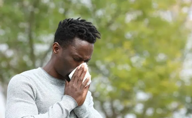 black man sneezing into a tissue while standing outside
